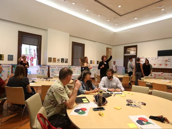 Campus constituents work around tables in a large room, and place post-it notes on the room's walls 