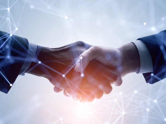 Two businesspeople shaking hands with a glowing, warm backlight and an overlay of IT-oriented lines and dots meant to convey interconnectivity