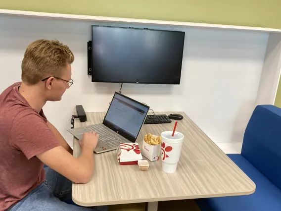 A student lunches while he works on his computer in the SUMC Tech Zone Lounge