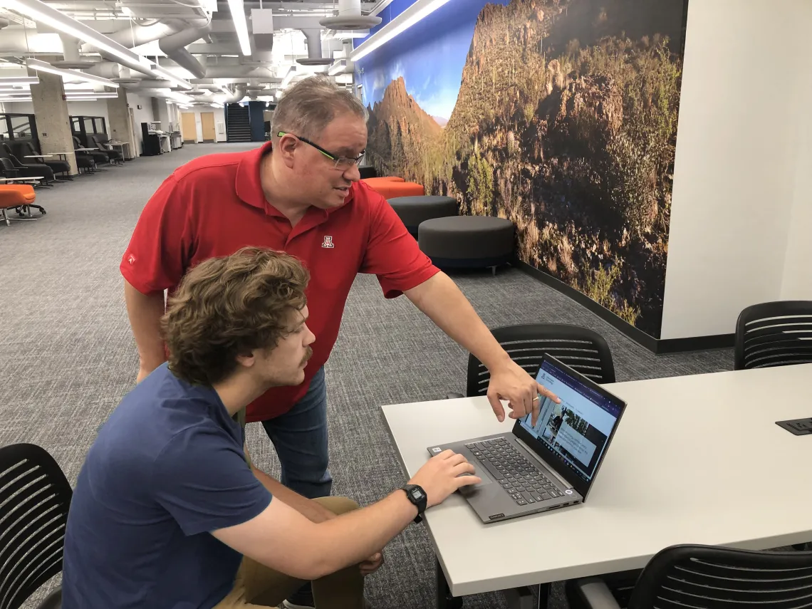 Tech points out info on a laptop in the 24/7 Lounge in the Library