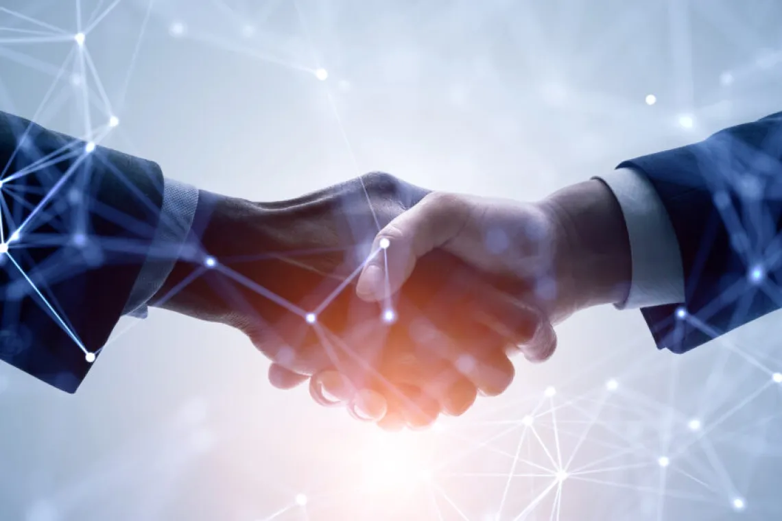 Two businesspeople shaking hands with a glowing, warm backlight and an overlay of IT-oriented lines and dots meant to convey interconnectivity